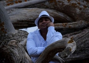 Pierre Gino au chapeau blanc, appuyé sur du bois flotté